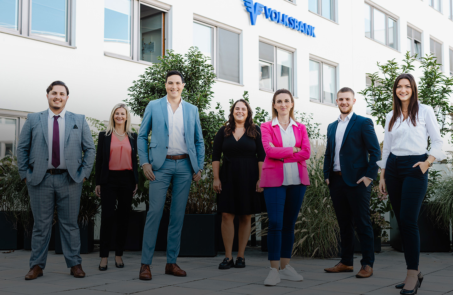 Eine Gruppe Volksbank Mitarbeiter:innen steht lächelnd im Innenhof der Volksbank Zentrale in Wien.