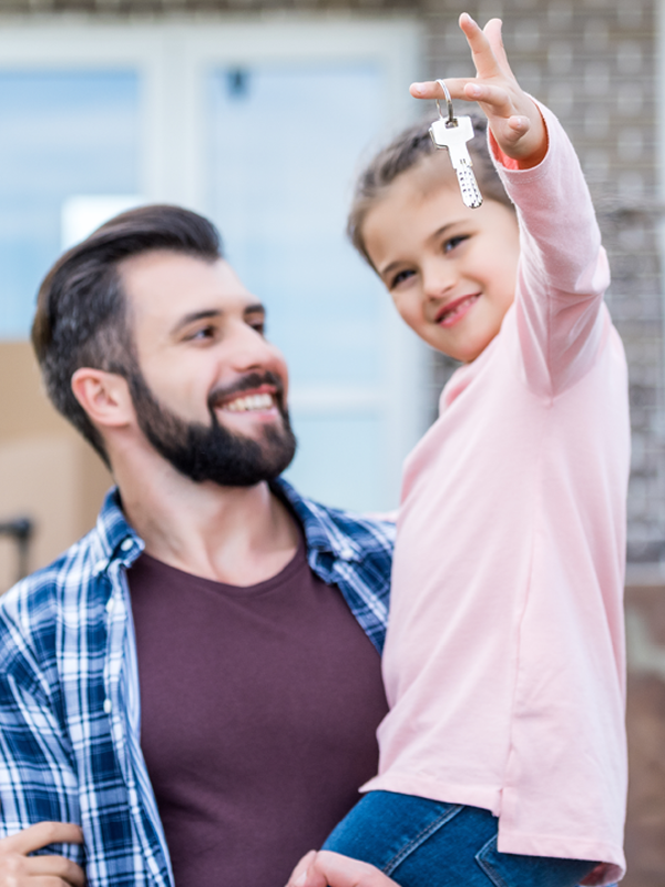 Eine junge Familie steht vor ihrem neuen Zuhause. Die Tochter hält einen Schlüssel in der Hand.