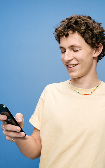 Ein Jugendlicher in gelbem T-Shirt schaut lächelnd auf sein Handy.