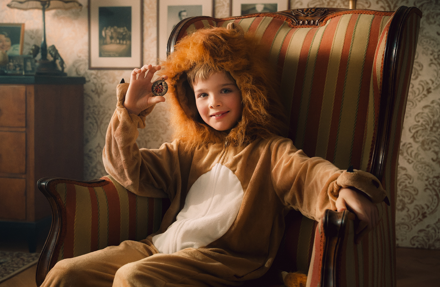 Ein kleiner Junge sitzt in einem Löwenkostüm auf einem Sessel und lächelt.