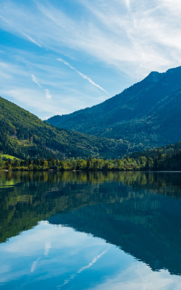 Im Vordergrund ein See, dahinter grün bewaldete Berge.
