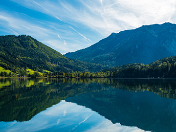 Im Vordergrund ein See, dahinter grün bewaldete Berge.