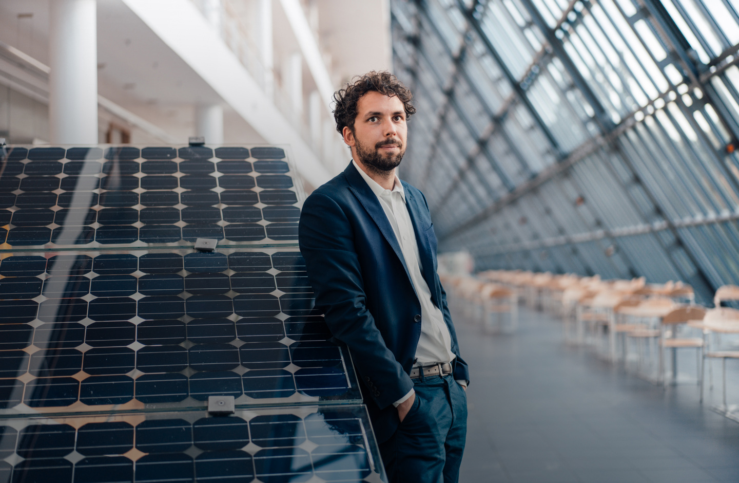 Ein junger Mann im Anzug steht in einer gläsernen Halle und lehnt sich an Solaranlagen.