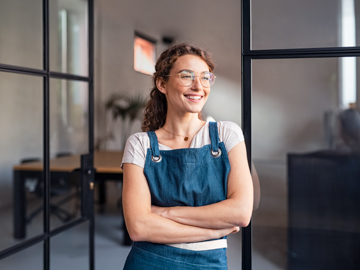 Eine Frau steht in einem Büro und verschränkt lächelnd die Arme.