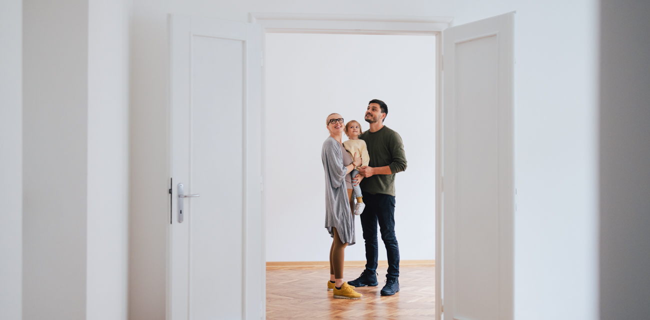 Eine junge Familie steht in ihrem neuen Zuhause und betrachten die leeren Räume.