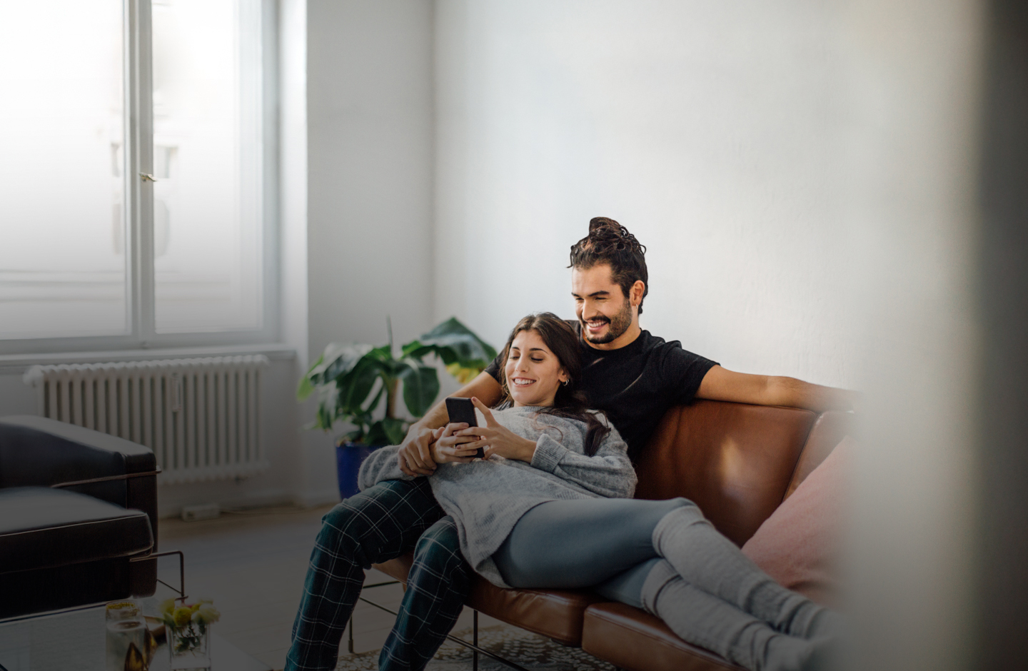 Eine Frau liegt auf einer Couch in den Armen eines Mannes und blickt auf ihr Handy.