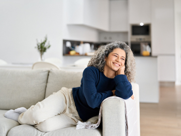 Eine Frau mit grauen haaren liegt auf einer Couch und lächelt.