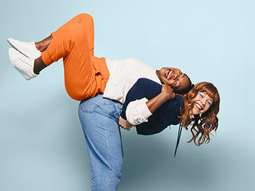 Zwei Teenagerin nehmen einander Huckepack auf hellblauem Hintergrund und lachen.