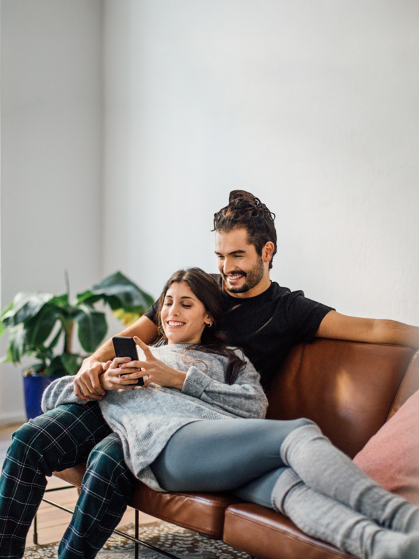 Ein junges Paar liegt auf einer Couch und blickt auf ein Mobiltelefon.