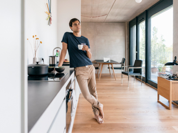 Ein Mann lehnt mit Kaffeetasse in der Hand lässig an einem Küchentresen.